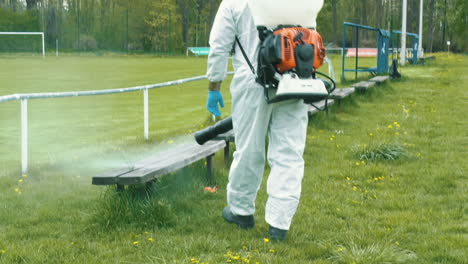 A-man-in-protective-equipment-disinfects-benches-on-the-football-stadium