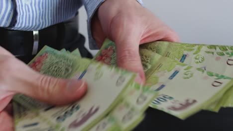 Young-businessman-counting-Argentine-cash-money-"pesos".-Close-up