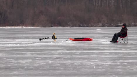 Un-Hombre-Está-Sentado-En-Una-Silla-Plegable-Junto-A-Su-Equipo-De-Pesca-En-Hielo-En-Un-Lago-Congelado