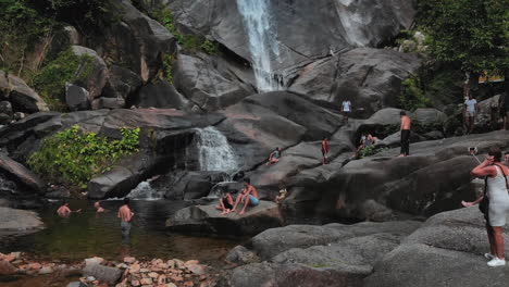 Eine-Menschenmenge-Entspannt-Sich-Am-Wasserfallsee-Eines-Beeindruckenden-Wasserfalls,-Der-Von-Roten-Felsen-Umgeben-Ist