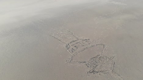 Aerial,-orbit,-drone-shot,-around-a-drawing-of-a-water-tower-in-sand,-at-a-beach,-in-Langeoog,-Germany