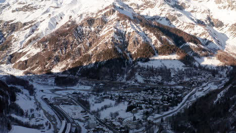 Aerial-tilt-up-from-small-town-in-valley-to-mountains-in-winter