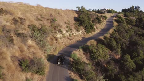 Toma-Aérea-Cinematográfica-De-Un-Jeep-Negro-Conduciendo-Por-Una-Carretera-Asfaltada-En-Las-Colinas-De-Los-ángeles