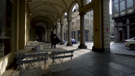 Empty-tables-on-arch-covered-pavement-and-people-passing-by