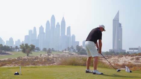 Hombre-Golpeando-Un-Disco-De-Golf-En-Un-Campo-De-Golf-Con-El-Horizonte-Del-Puerto-Deportivo-De-Dubai-Al-Fondo