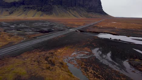 Aerial-4k-view-of-an-Icelandic-road-with-a-bridge-over-a-glacial-river-and-a-beautiful-mountain-background,-Iceland,-Europe,-Establishing-tilt-up-shot