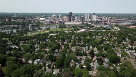 Wide-aerial-shot-slowly-moving-upwards-with-the-city-of-Saint-Paul,-Minnesota-on-the-horizon-next-to-the-Mississippi-river-surrounded-by-trees-and-houses-on-a-sunny-day