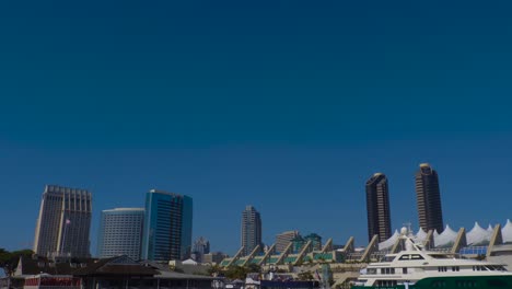 Embarcadero-area-with-Hornblower-boat-and-yacht-with-the-convention-center-and-Hyatt-hotel-in-the-background,-Tilt-down-from-the-sky-shot