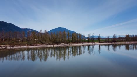A-zoom-drone-shot-towards-mountains-in-Mission,-BC,-Canada-over-the-Fraser-River-on-a-blue-cloudy-day