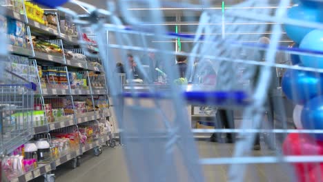 Queueing-customers-at-cash-desk-in-supermarket-with-balloons-on-the-side-and-store-rack,-wide-shot