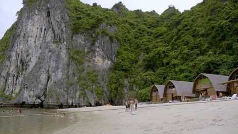 Touristen-Genießen-Einen-Spaziergang-Am-Sandstrand-Von-Ha-Long-Bay,-Vietnam-Mit-Der-Wunderschönen-Kalksteinfelsenformation-Im-Hintergrund---Weite-Schwenk