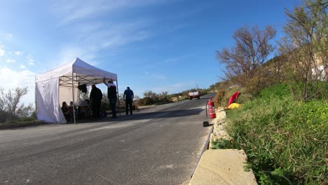 Hombres-En-El-Trabajo-Reunidos-En-La-Tienda-Junto-A-La-Parada-En-Boxes-En-La-Colina-En-Imtahleb-Malta-Con-Extintor-De-Incendios-Al-Lado-De-La-Carretera---Lapso-De-Tiempo-De-Gopro