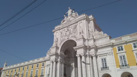 Pan-down-shot-of-Rua-Augusta-Arch-with-red-tram-passing-by-in-Lisbon-Portugal
