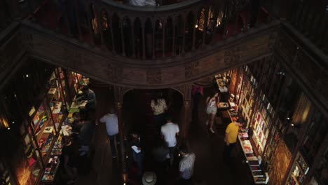 Tilt-down-from-beautiful-ceiling-of-Livaria-Lello-bookstore-in-Porto,-Portugal-past-ornate-staircase-to-people-shopping-lower-floor