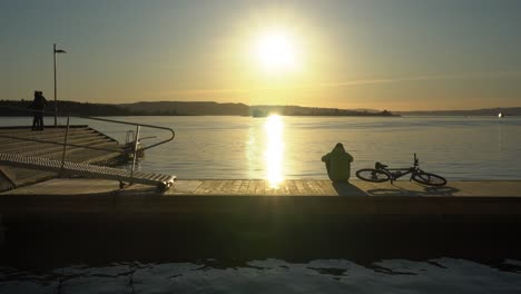 Persona-Con-Silueta-De-Bicicleta-Contemplando-La-Puesta-De-Sol-Sobre-El-Fiordo-De-Oslo-Desde-El-Puerto