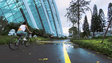 Mujeres-En-Bicicleta-En-La-Ruta-De-Bicicletas-Mojadas-En-La-Cúpula-De-Flores-En-Singapur---Tiro-Lento-En-Camión