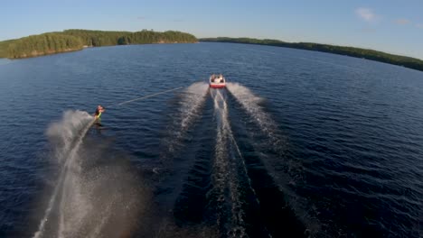 Caucasian-Man-Slalom-Water-Skis-behind-White-Boat-on-Blue-Lake-in-Summer-Sunset-Light,-FPV-Drone-Aerial-Orbit-and-Follow