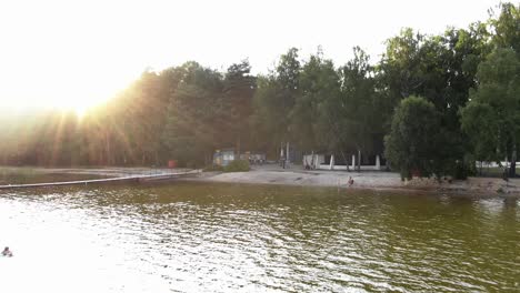 Aerial-View-of-People-Walking-in-Park-Tracking-Out-Revealing-Lake-During-Sunset