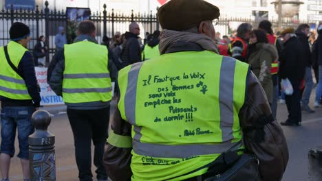 An-old-man-with-a-french-hat-and-a-yellow-jacket-observes-the-demonstration-in-France-wearing-a-yellow-jacket-with-a-quote-from-Abbé-Pierre
