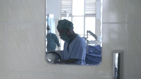 Foto-De-Trípode-Con-Reflejo-De-Espejo-De-Un-Médico-Preparando-Sus-Herramientas-Para-La-Cirugía-En-Un-Hospital-Clínico-Vistiendo-Un-Mono-Azul-Con-Una-Cubierta-Bucal