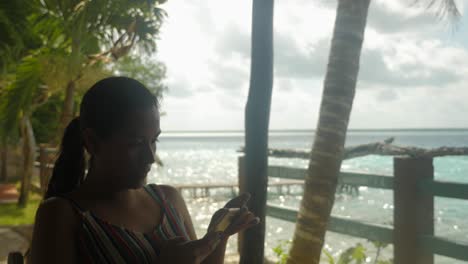 Woman-checking-her-phone-in-the-shade-with-sunny-lagoon-on-background