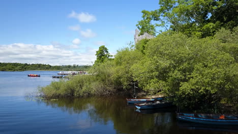 Kleines-Ausflugsboot-Verlässt-Die-Küste,-Während-Die-Luftbildkamera-Tief-über-Dem-Wasser-Schwenkt-Und-An-Einem-Sonnigen-Sommertag-Das-Historische-Schloss-Enthüllt