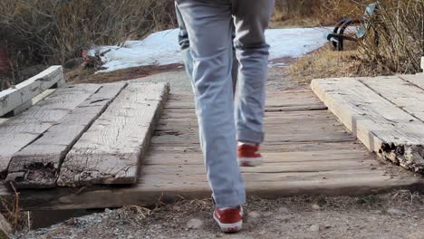 Two-men-walk-across-footbridge-in-park-during-winter-one-clicks-heels