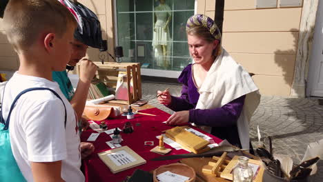 Slow-motion-of-a-peasant-commoner-women-selling-scribes-and-scroll-to-children-in-the-market,-Medieval-reenactment,-Preludij-festival-in-Slovenj-Gradec-slovenia