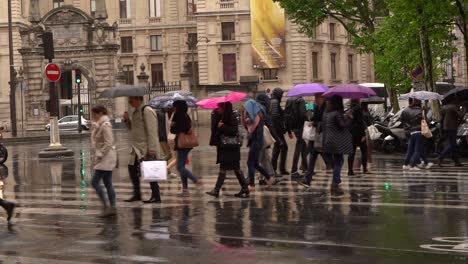 People-using-umbrellas-crossing-an-avenue-on-a-rainy-day-in-Paris,-France