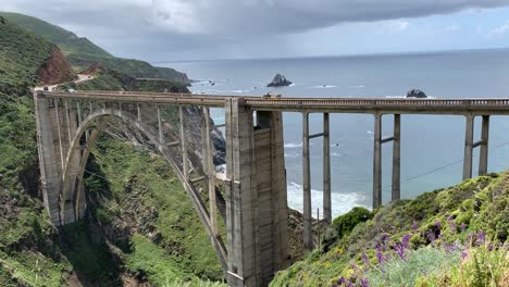 A-young-couple-enjoying-the-sweeping-views-of-the-Big-Sur-coastline-on-Bixby-Creek-Bridge,-one-of-the-most-frequently-photographed-bridges-in-the-West-Coast-and-perhaps-even-the-world