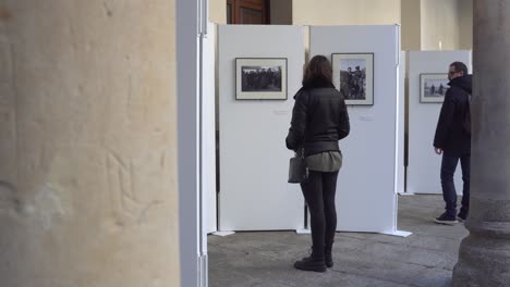 Salamanca,-Spanien---7.-Dezember-2019:-Menschen-Beobachten-Eine-Städtische-Ausstellung-Auf-Der-Plaza-De-Salamanca,-Schöne-Frau-Mit-Bokeh-Hinter-Den-Säulen-Beobachtet-Die-Werke