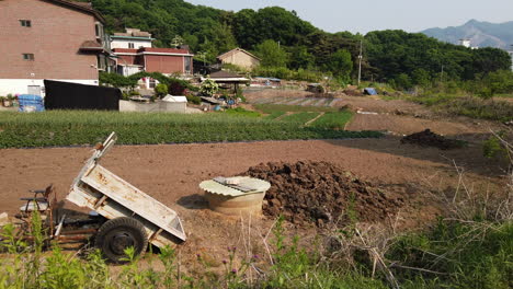 Koreanischer-Bauernhof-Mit-Schubkarre-Im-Vordergrund-Und-Bergen-Im-Hintergrund