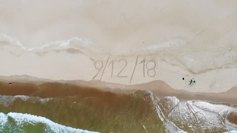 Top-down-aerial-of-writing-in-the-sand-of-a-beach