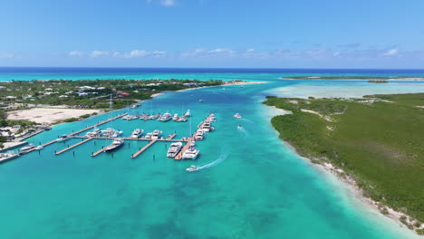 Push-in-aerial-4K-footage-of-a-marina-with-boats-cruising-in-blue-waters,-stationary-yachts,-and-green-land-with-resorts-under-a-clear-blue-sky-in-Turks-and-Caicos