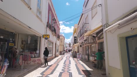 Sunny-day-on-a-narrow-street-with-shops-and-people-in-Lagos,-Portugal