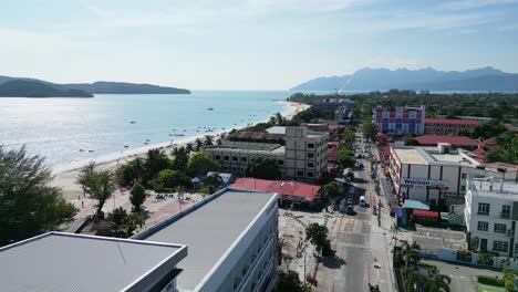 -Stunning-aerial-view-of-a-coastal-city-in-Malaysia-showcasing-beautiful-beaches,-cityscape,-and-distant-mountains-under-a-clear-blue-sky