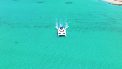 Tilt-down-shot-focusing-on-white-yacht-with-people,-cruising-on-clear-blue-waters