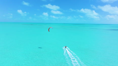 Circling-shot-shows-a-kite-surfer-cruising-forward-on-the-stunning-blue-waters-with-an-orange-kite