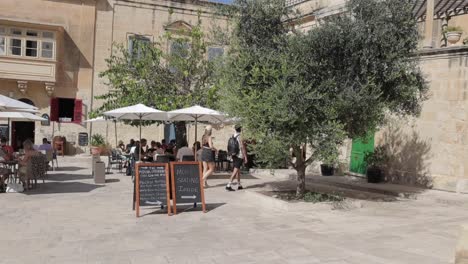 Travelers-and-visitors-traverse-the-streets-and-café-shops-of-Mdina,-Malta,-on-a-sunny-day,-capturing-the-essence-of-leisurely-exploration-and-vibrant-local-culture