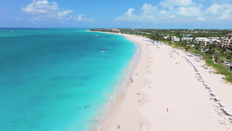 Downward-aerial-4K-footage-of-Grace-Bay-coastline-with-white-sand,-turquoise-waters,-sunbathers,-and-swimmers