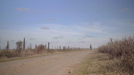 Low-angle-view-of-a-man-walking-towards-the-camera-over-a-dirt-road-in-a-rural-setting