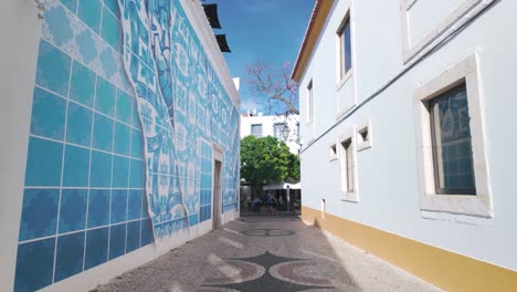 A-narrow-alley-in-Lagos,-Portugal-with-patterned-pavement-and-blue-tiled-walls-on-a-sunny-day