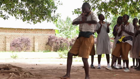 Children-dancing-energetically-in-a-schoolyard-in-Kampala,-Uganda-under-a-large-tree