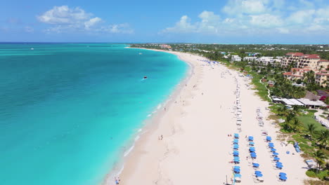 Pull-back-aerial-4K-footage-revealing-the-stunning-coastline-of-Grace-Bay-Beach-with-white-sandy-shores,-blue-waters,-and-green-coastal-resorts