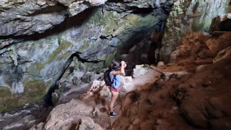 Athletic-hiking-woman-taking-pictures-with-camera-inside-a-cave