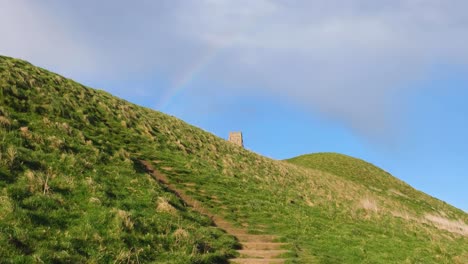 A-colourful-rainbow-arching-over-St-Michael's-Tower-on-The-Tor-in-Glastonbury,-Somerset,-England-UK