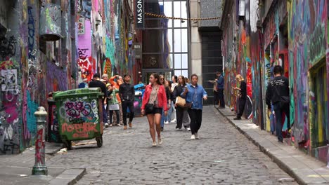 Turistas-Recorriendo-Hosier-Lane-En-La-Ciudad-De-Melbourne,-Una-Popular-Callejuela-Adoquinada-Con-Una-Vibrante-Variedad-De-Murales-Artísticos-Y-Graffiti-En-Las-Paredes-Exteriores-De-Los-Edificios,-Una-Escena-Callejera-Cultural-Creativa