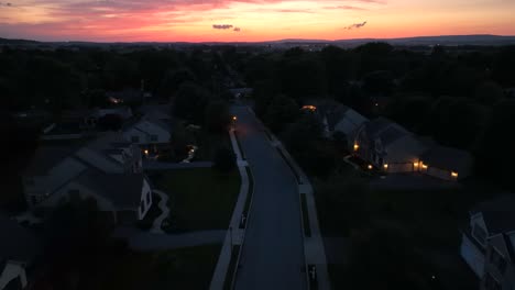 Aerial-backwards-shot-of-a-quiet-suburban-neighborhood,-illuminated-by-streetlights-and-house-lights-in-USA