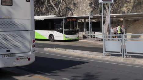 En-La-Estación-De-Autobuses-De-La-Valeta,-Malta,-Hay-Autobuses-Estacionados-Para-Recoger-A-Los-Viajeros-Mientras-Otros-Pasan,-Lo-Que-Ilustra-El-Bullicioso-Centro-De-Transporte-Y-La-Vida-De-Los-Viajeros.