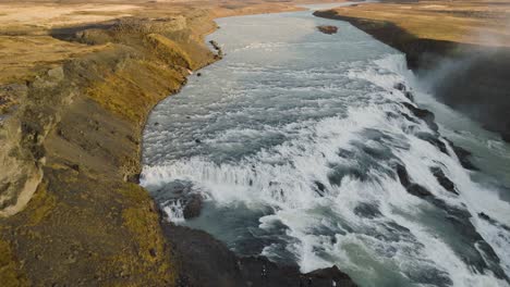 Impresionante-Vista-Aérea-De-Una-Majestuosa-Cascada-Que-Cae-A-Través-De-Un-Río-Islandés,-Capturando-La-Cruda-Belleza-De-La-Naturaleza-Desde-Arriba